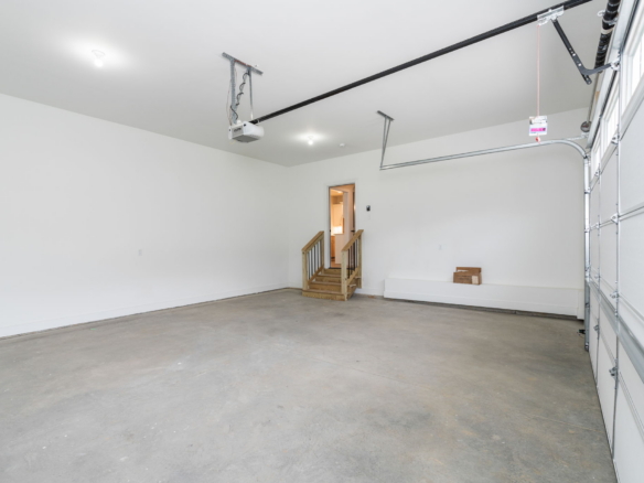 Empty residential garage with a concrete floor, white walls, and an overhead garage-door opener mounted to ceiling rails
