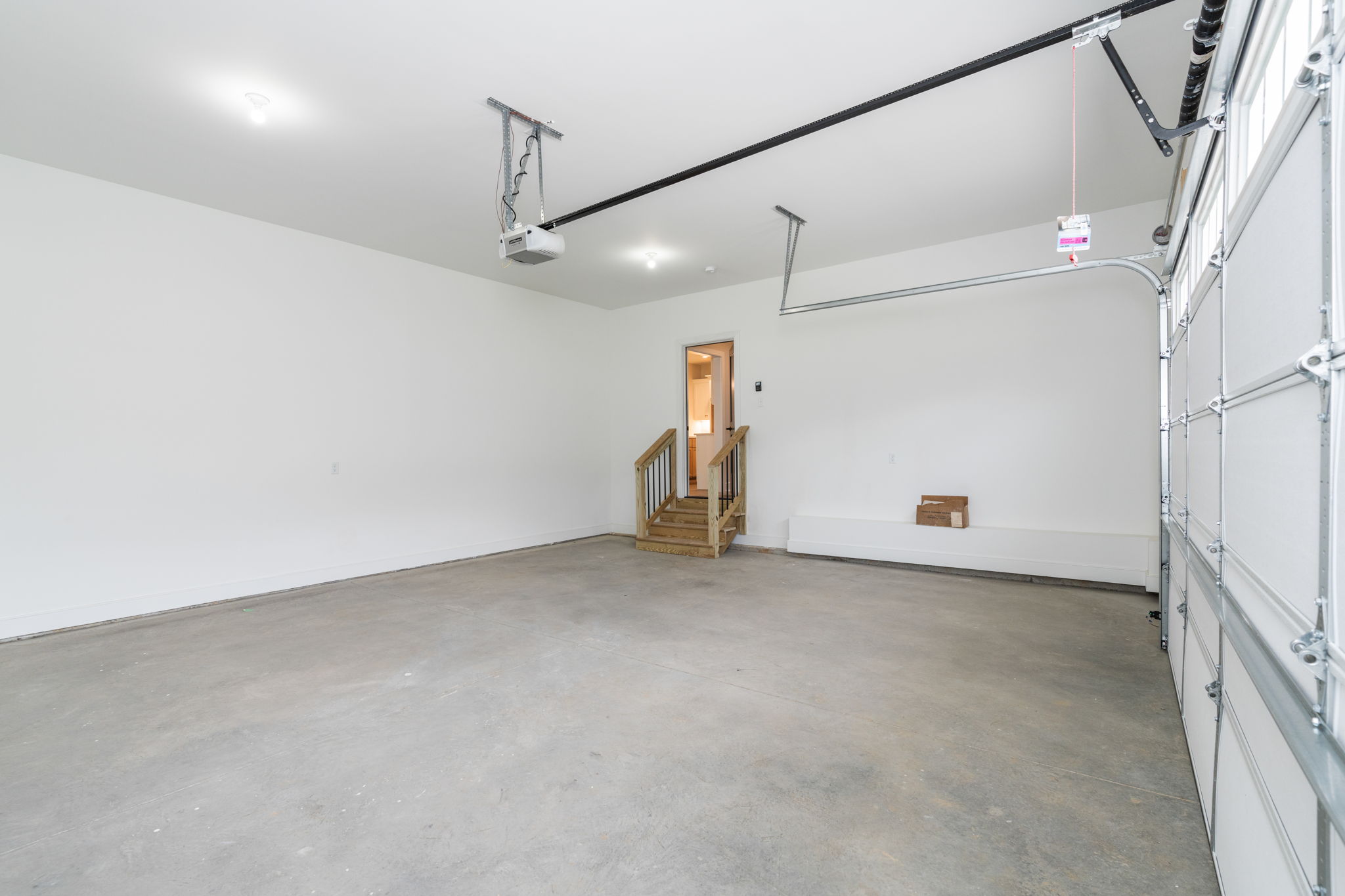 Empty residential garage with a concrete floor, white walls, and an overhead garage-door opener mounted to ceiling rails