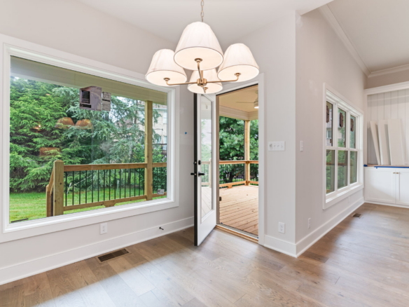 Interior dining area with a white multi-armed chandelier and large windows showing a wooden deck and green backyard outside.