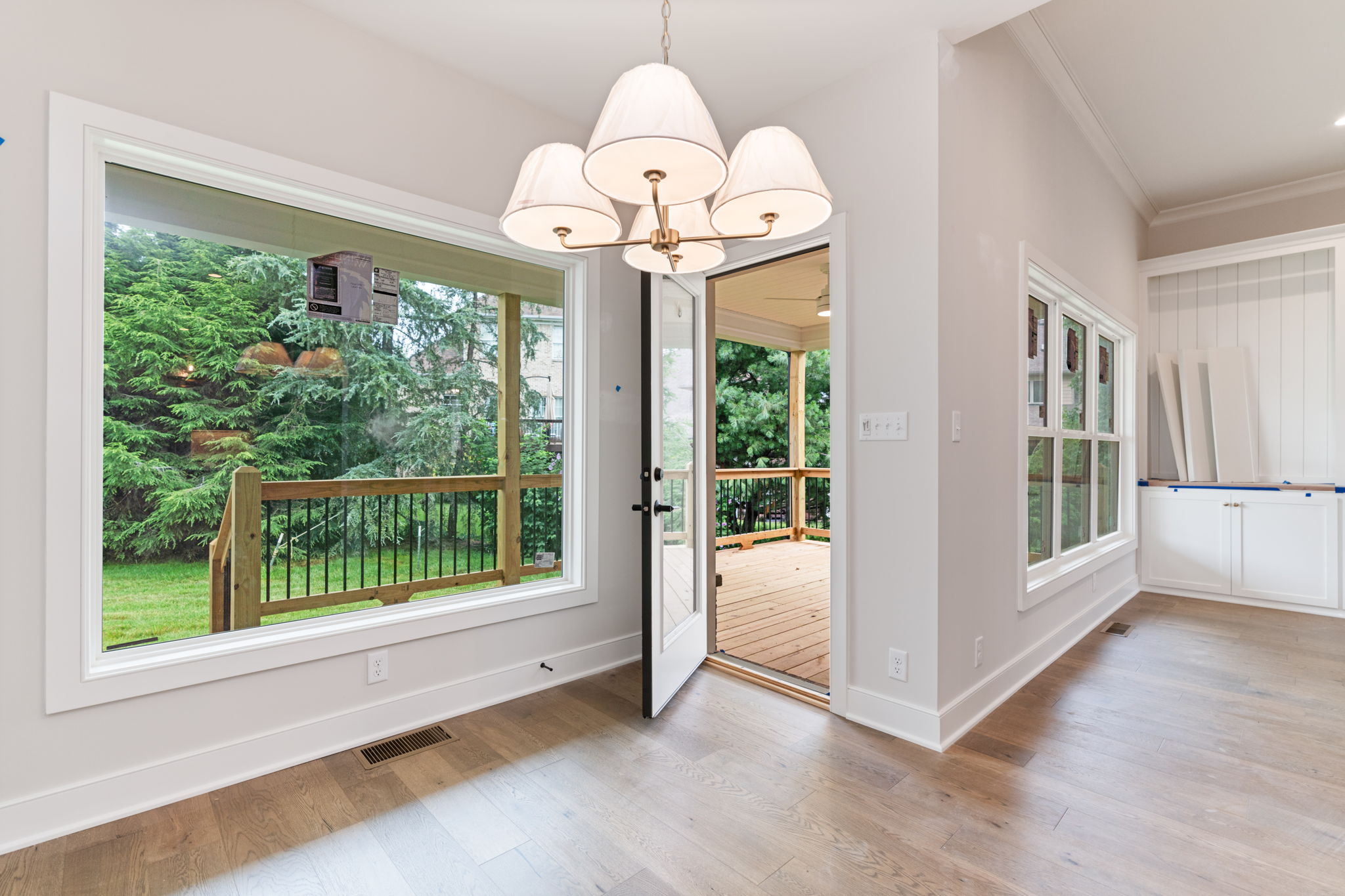 Interior dining area with a white multi-armed chandelier and large windows showing a wooden deck and green backyard outside.
