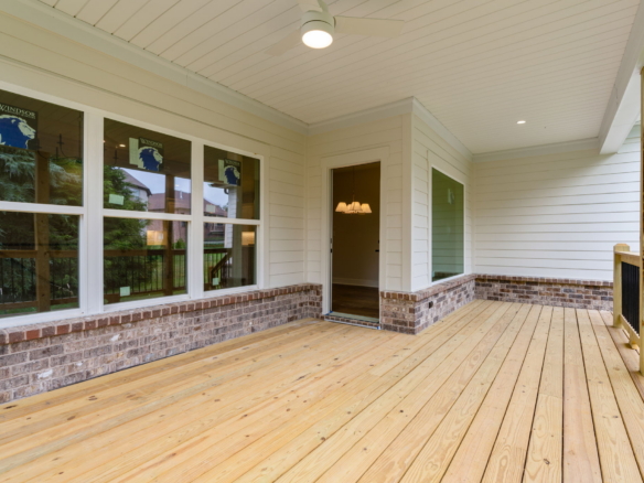 Covered wooden porch with brick base, large windows, and an open door revealing a chandelier inside.