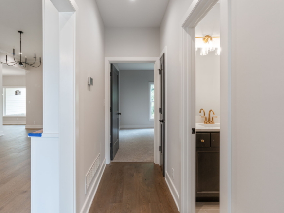 Bright white hallway with multiple door frames; a bathroom with a gold faucet is visible to the right.