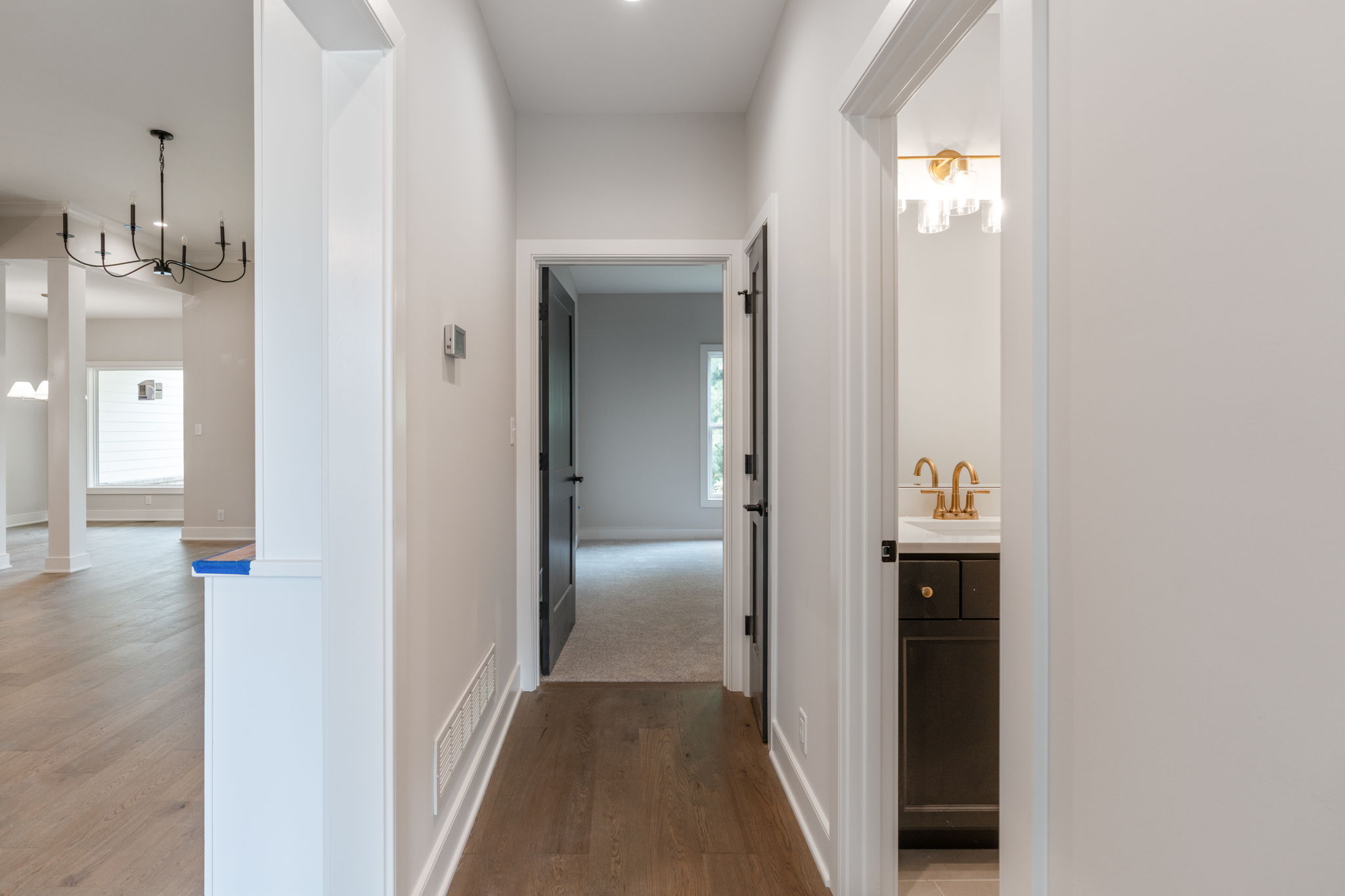 Bright white hallway with multiple door frames; a bathroom with a gold faucet is visible to the right.