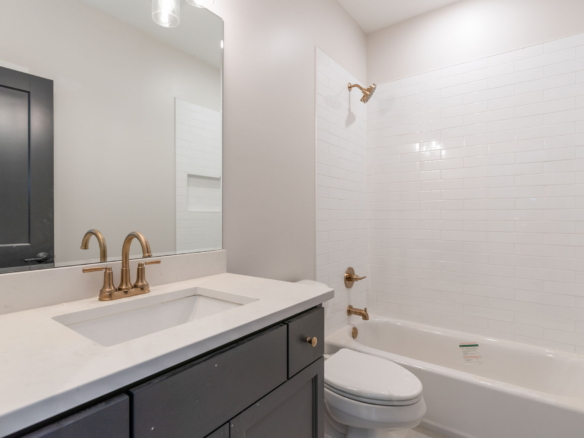 Modern bathroom with a white countertop, gold faucet, dark vanity, large mirror, and white tiled shower area.