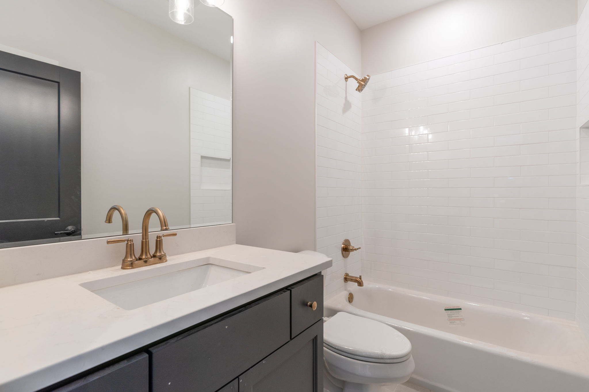 Modern bathroom with a white countertop, gold faucet, dark vanity, large mirror, and white tiled shower area.