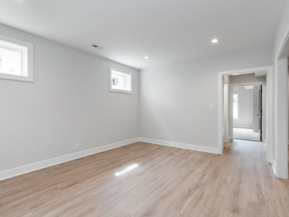 Empty modern room with light gray walls, wood flooring, and small rectangular windows bringing in natural light from the left side.