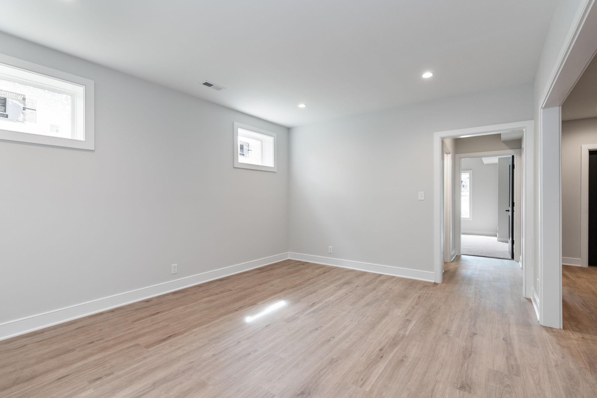 Empty modern room with light gray walls, wood flooring, and small rectangular windows bringing in natural light from the left side.