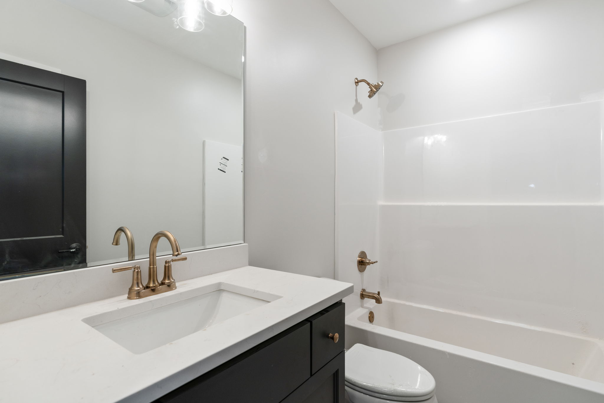 Modern bathroom with a white countertop, black vanity, and brass faucet beneath a large mirror.