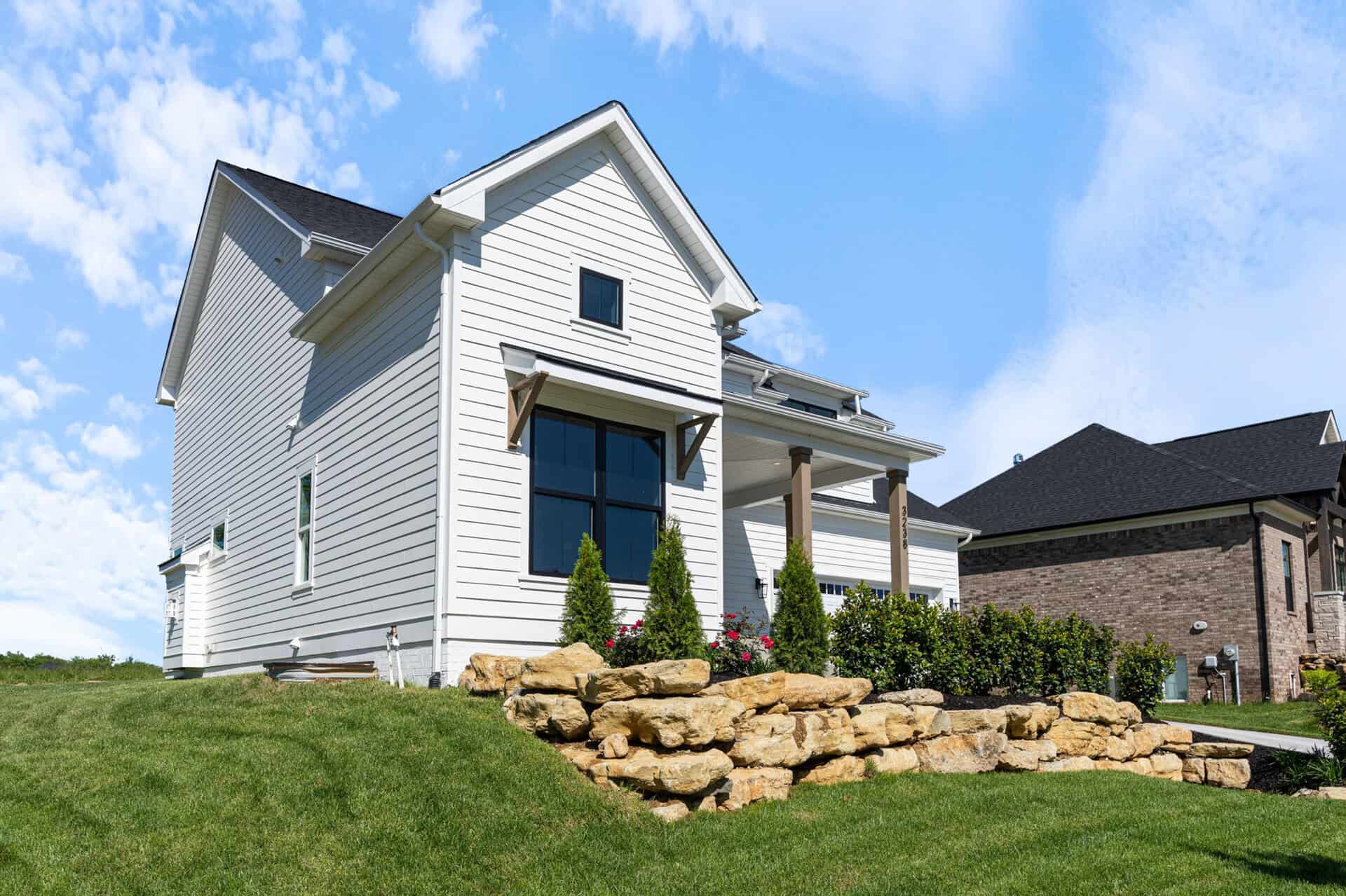 Modern white house with front porch, landscaped yard, and blue sky.