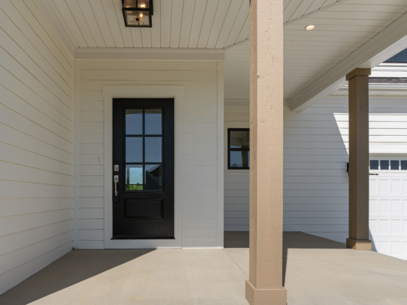 Front entry of a house with a black paneled door, white siding, and beige porch column under a covered porch.