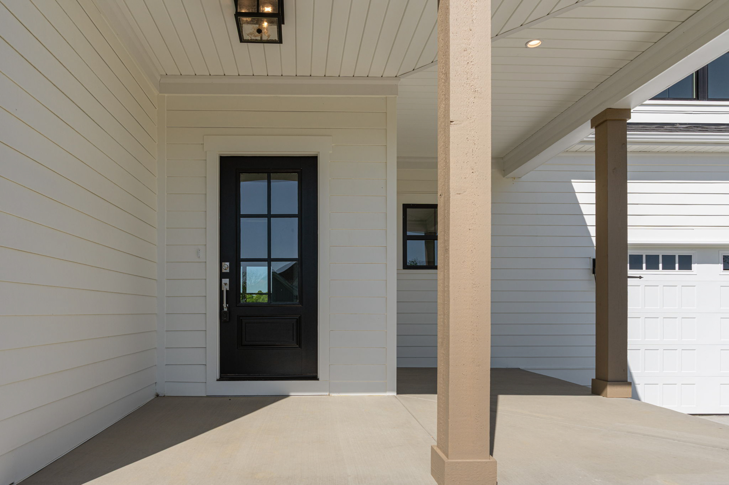 Front entry of a house with a black paneled door, white siding, and beige porch column under a covered porch.