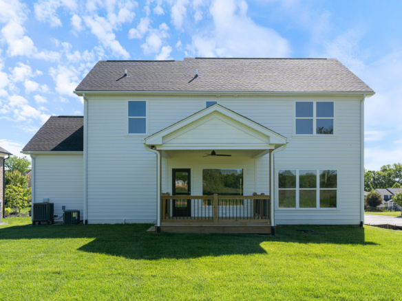 Two-story beige suburban house with a covered front porch and large windows under a blue sky.