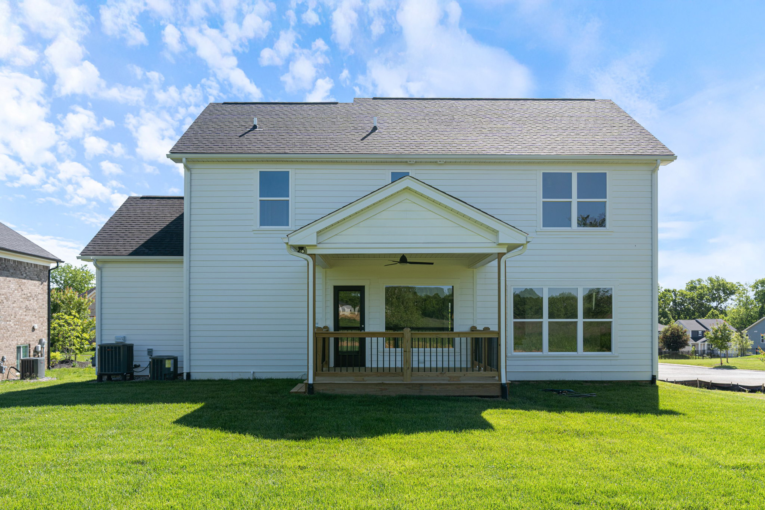 Two-story beige suburban house with a covered front porch and large windows under a blue sky.