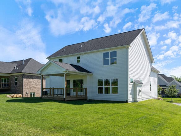 Modern white two-story house with a deck and large windows in a green yard.