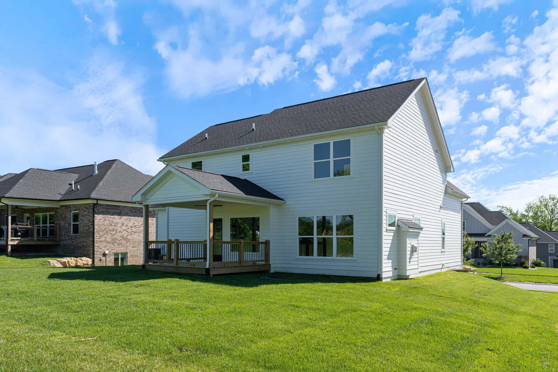 Modern white two-story house with a deck and large windows in a green yard.