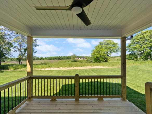 View from a covered porch overlooking a green field and trees under a blue sky.