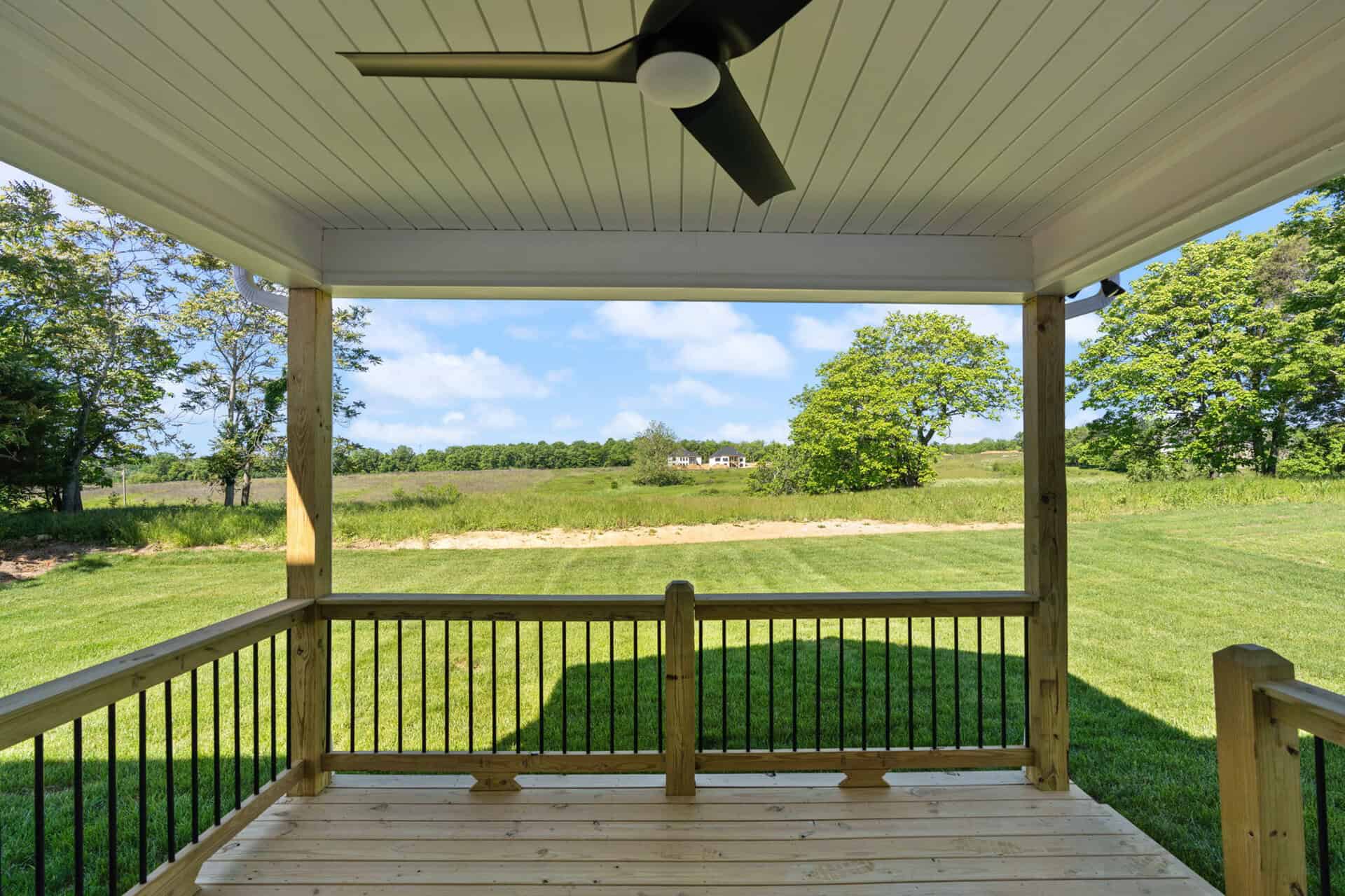 View from a covered porch overlooking a green field and trees under a blue sky.
