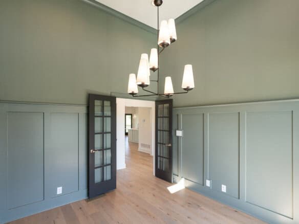 Elegant room with green walls, wooden floors, and modern chandelier lighting.
