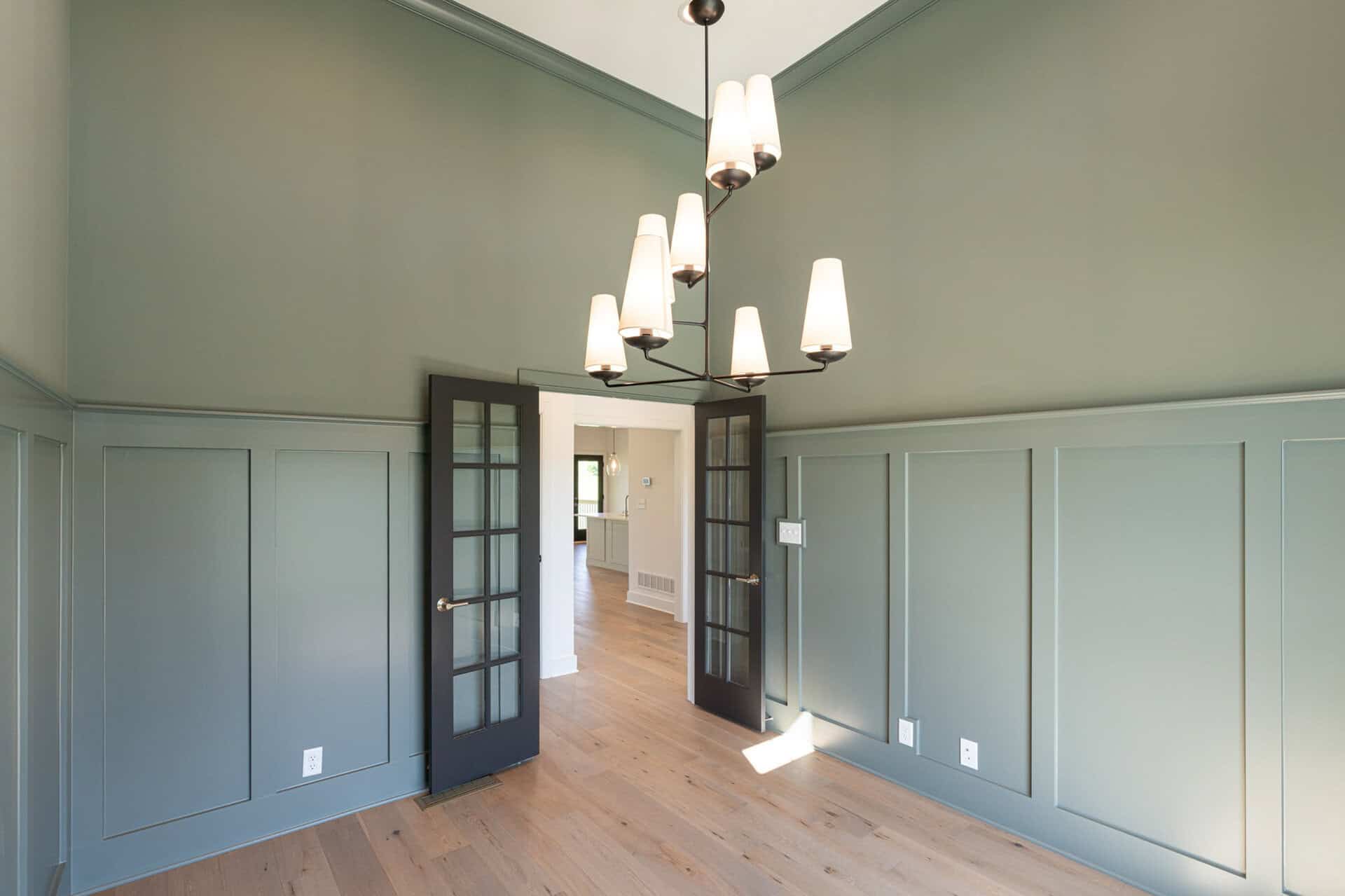 Elegant room with green walls, wooden floors, and modern chandelier lighting.