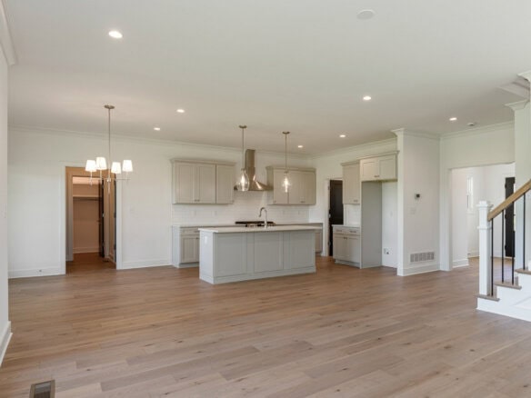 Open-concept kitchen with light gray cabinets, island, pendant lights, and hardwood floors in a bright home interior.