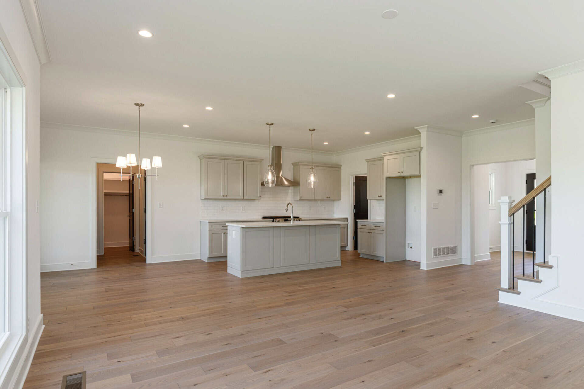 Open-concept kitchen with light gray cabinets, island, pendant lights, and hardwood floors in a bright home interior.