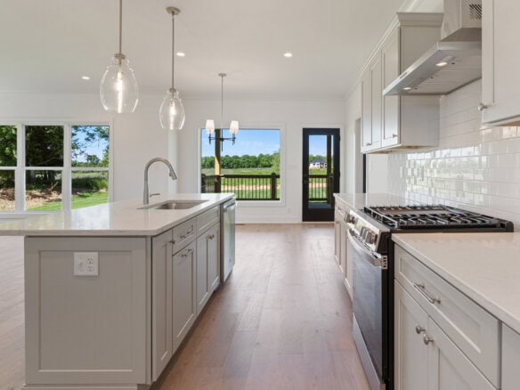 Modern kitchen with white cabinets, island, and large windows overlooking outdoors.