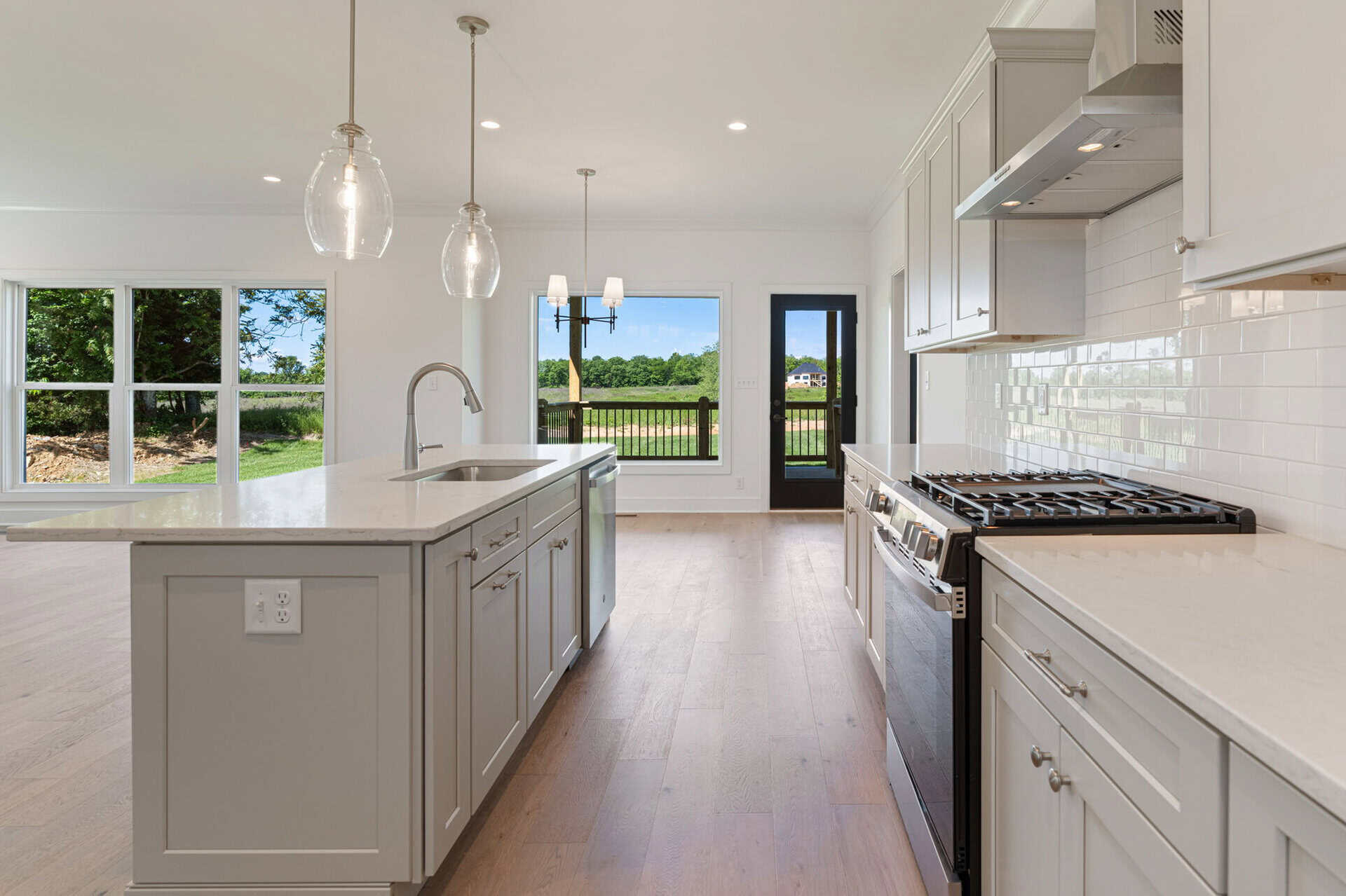 Modern kitchen with white cabinets, island, and large windows overlooking outdoors.