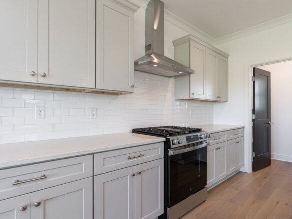 Modern kitchen with gray cabinets, white tile backsplash, and a stainless steel range hood above a gas stove.