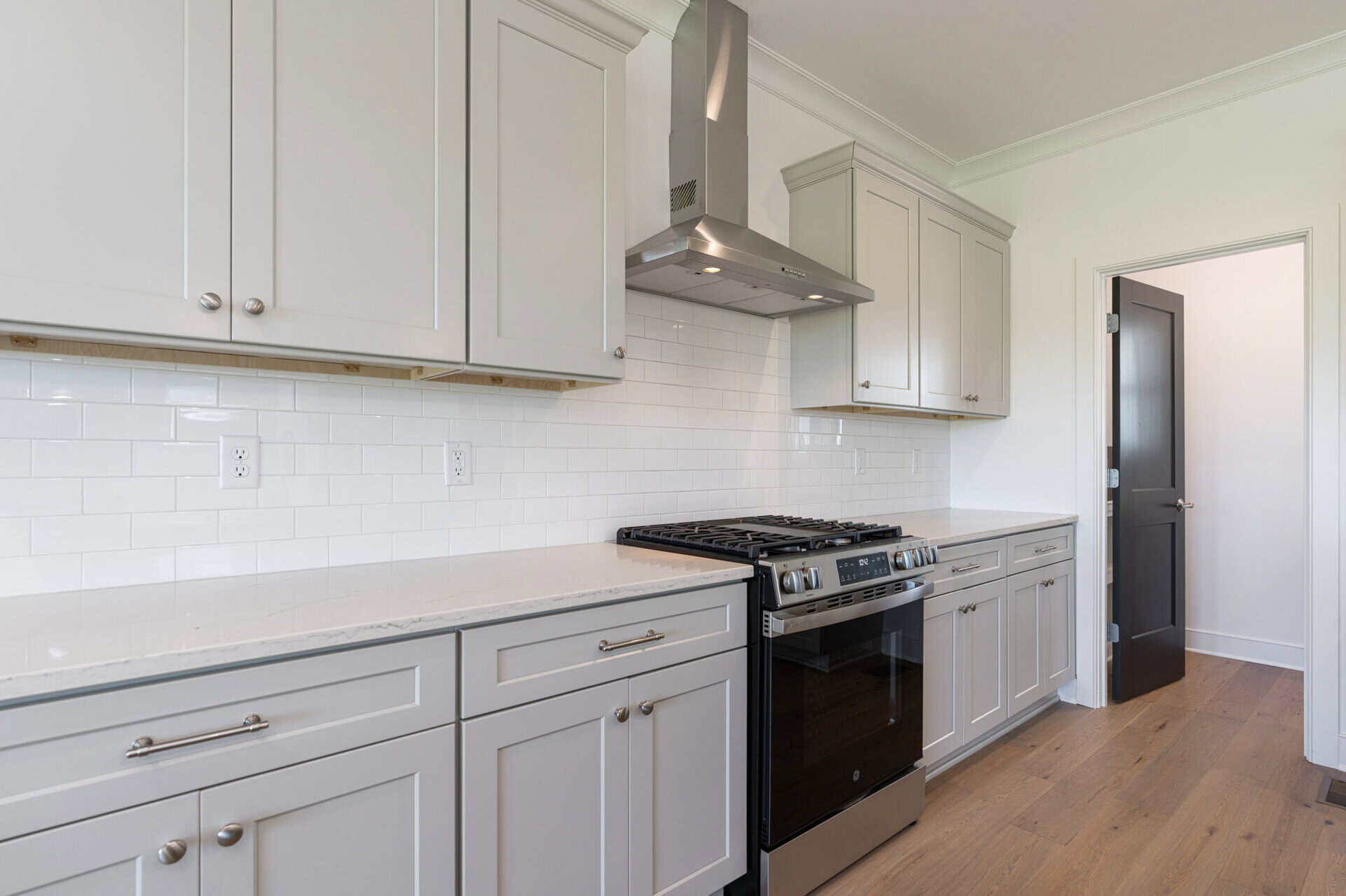 Modern kitchen with gray cabinets, white tile backsplash, and a stainless steel range hood above a gas stove.