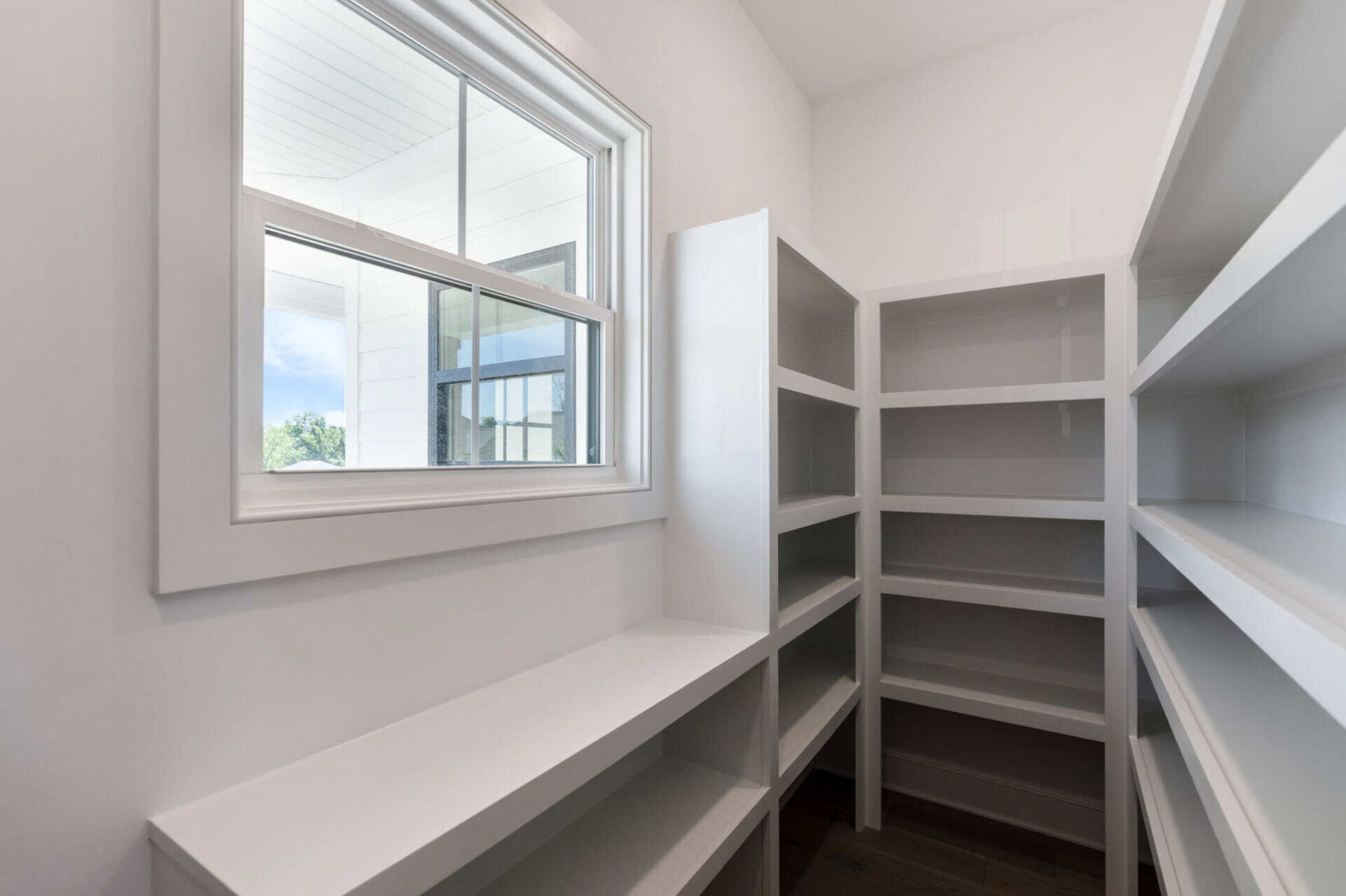 Empty white pantry with shelves and a window in a modern home.