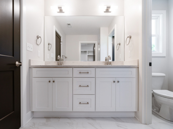 White bathroom vanity with double sinks, marble countertop, and large mirror with two wall lights above.