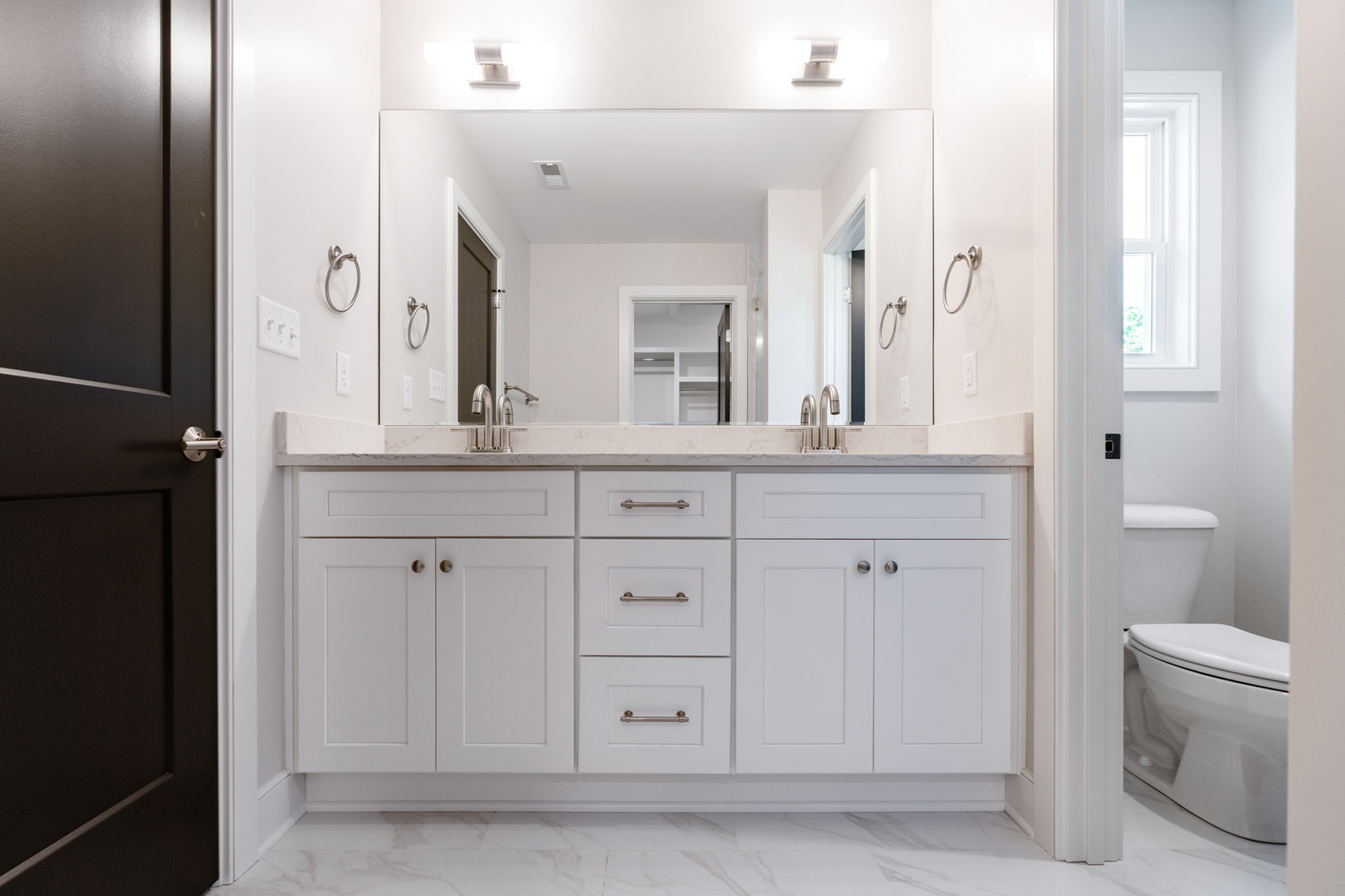 White bathroom vanity with double sinks, marble countertop, and large mirror with two wall lights above.