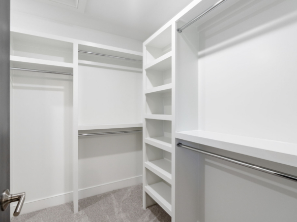 Walk-in white closet with shelving units and double hanging rods along the walls; carpeted floor under bright lighting.