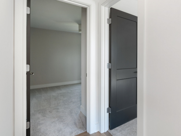 Opening to a carpeted room with gray walls and white trim, seen through an open doorway; a dark paneled door is on the right side of the frame.