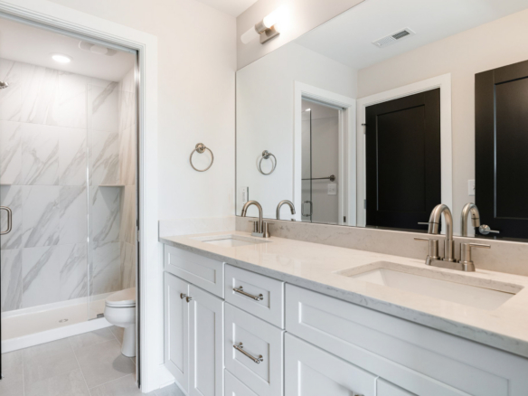 Double-sink bathroom vanity with marble countertop and large mirror, adjacent glass-enclosed shower.