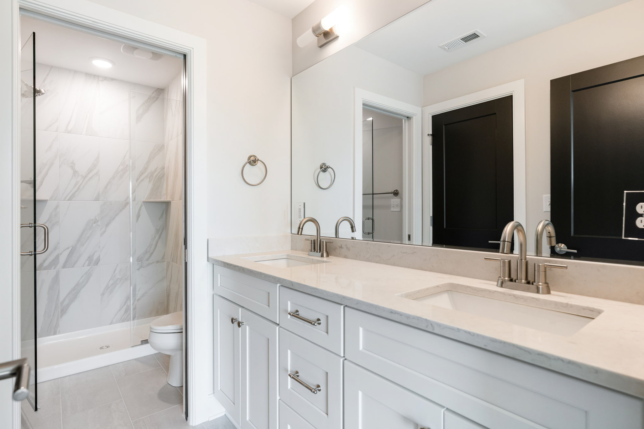 Double-sink bathroom vanity with marble countertop and large mirror, adjacent glass-enclosed shower.