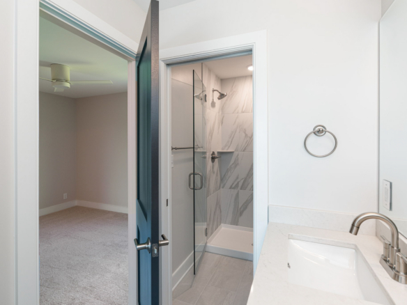Bathroom with a glass-enclosed shower and marble-tiled walls visible from the sink area; towel ring on the wall and quartz countertop nearby.