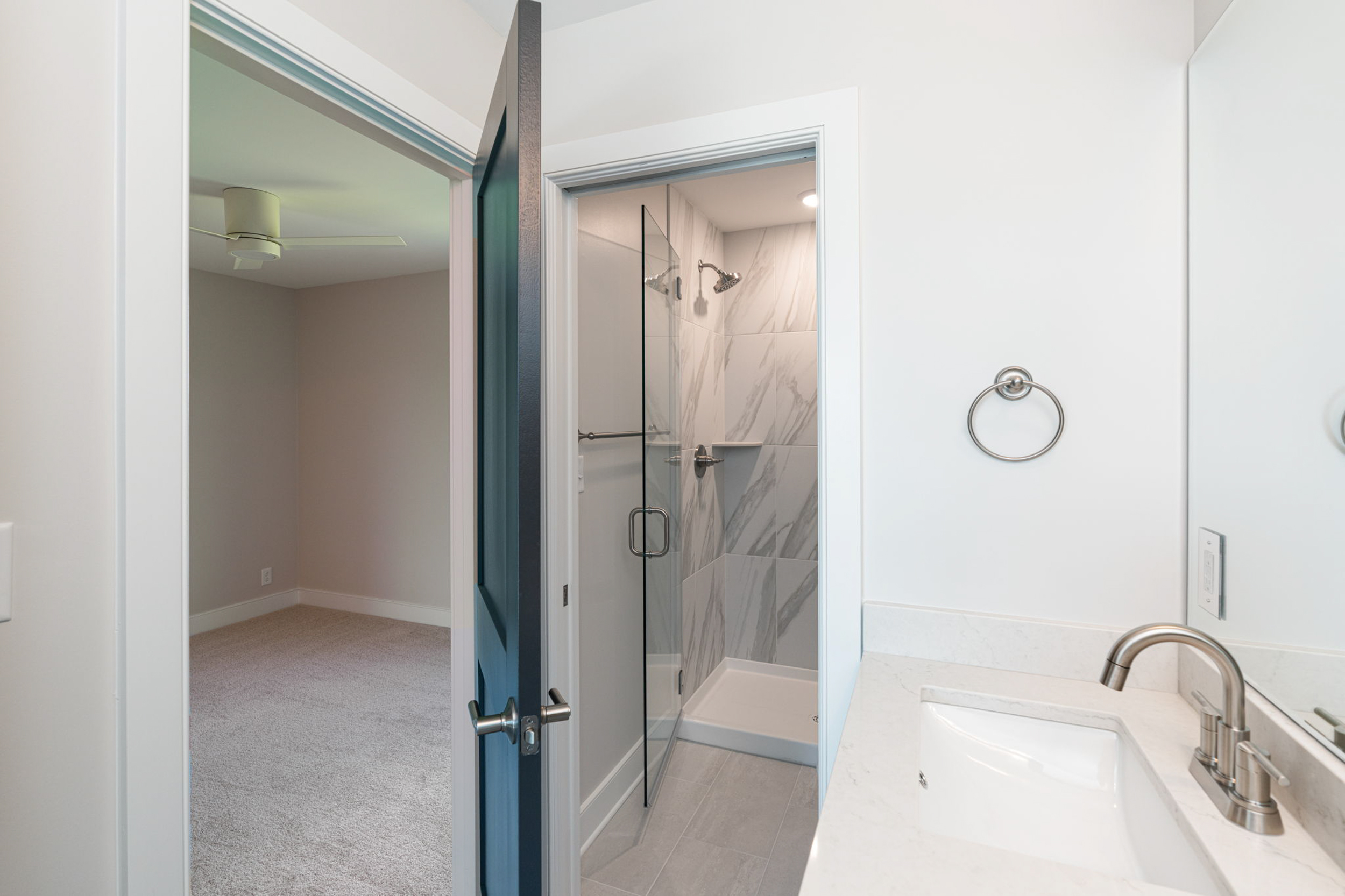 Bathroom with a glass-enclosed shower and marble-tiled walls visible from the sink area; towel ring on the wall and quartz countertop nearby.