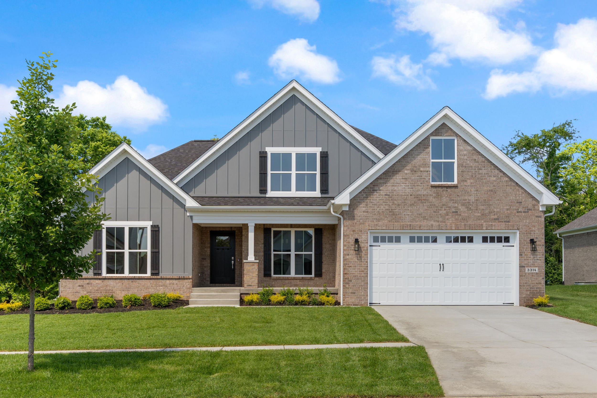 Photography by AS Media Co Front view of a brick-and-gray siding two-story house with a two-car garage and a green lawn under a blue sky.