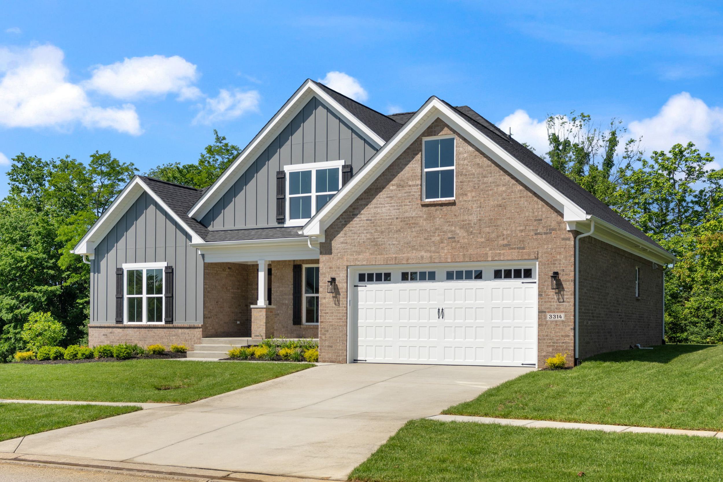 Front view of a suburban house with brick and gray siding, two peaked roofs, and a white two-car garage under a blue sky.