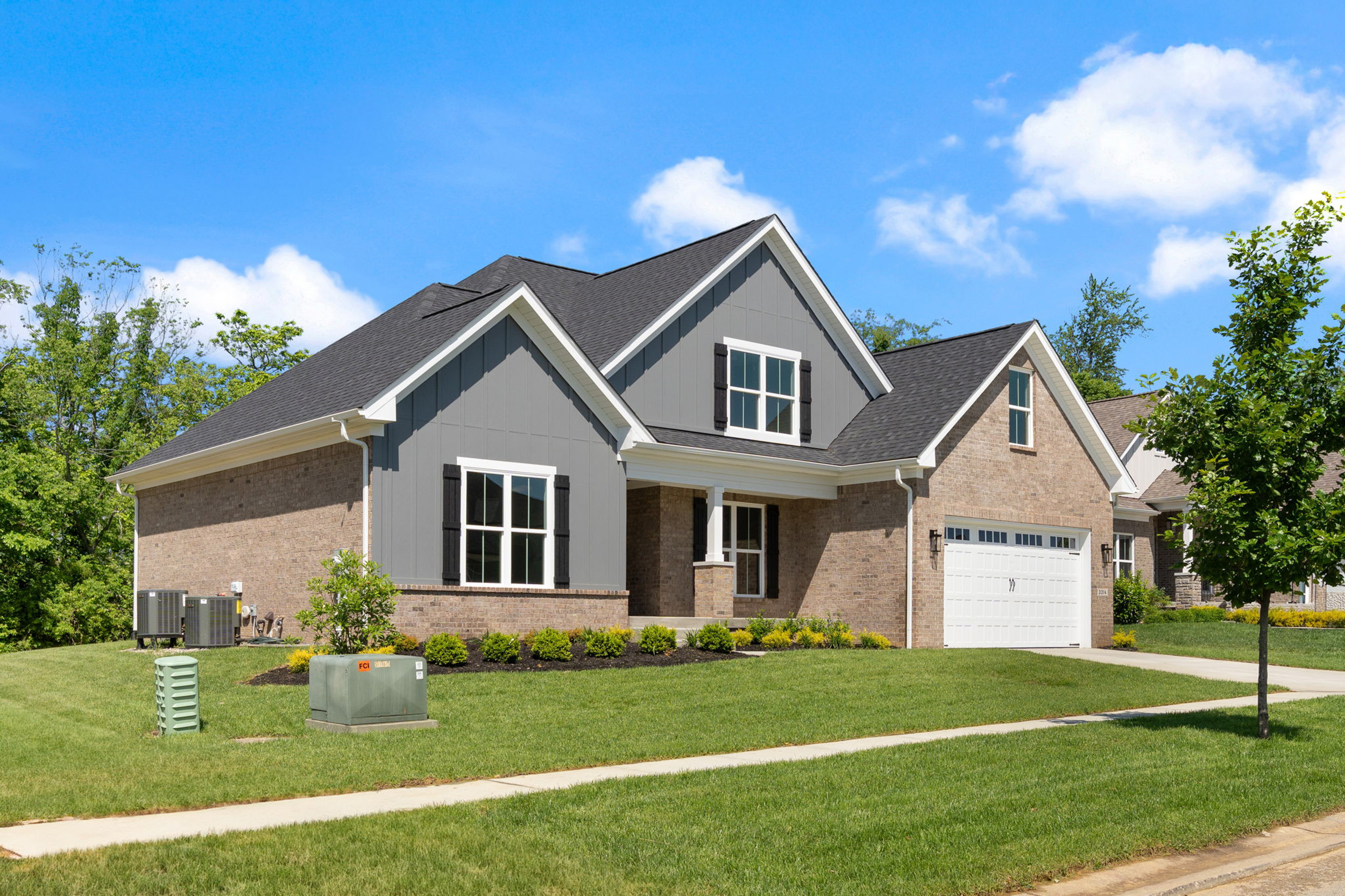 Front view of a two-story brick house with gray siding, white trim, and a double garage under a blue sky.