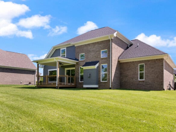 Modern brick home with a spacious backyard and a covered porch under a blue sky.