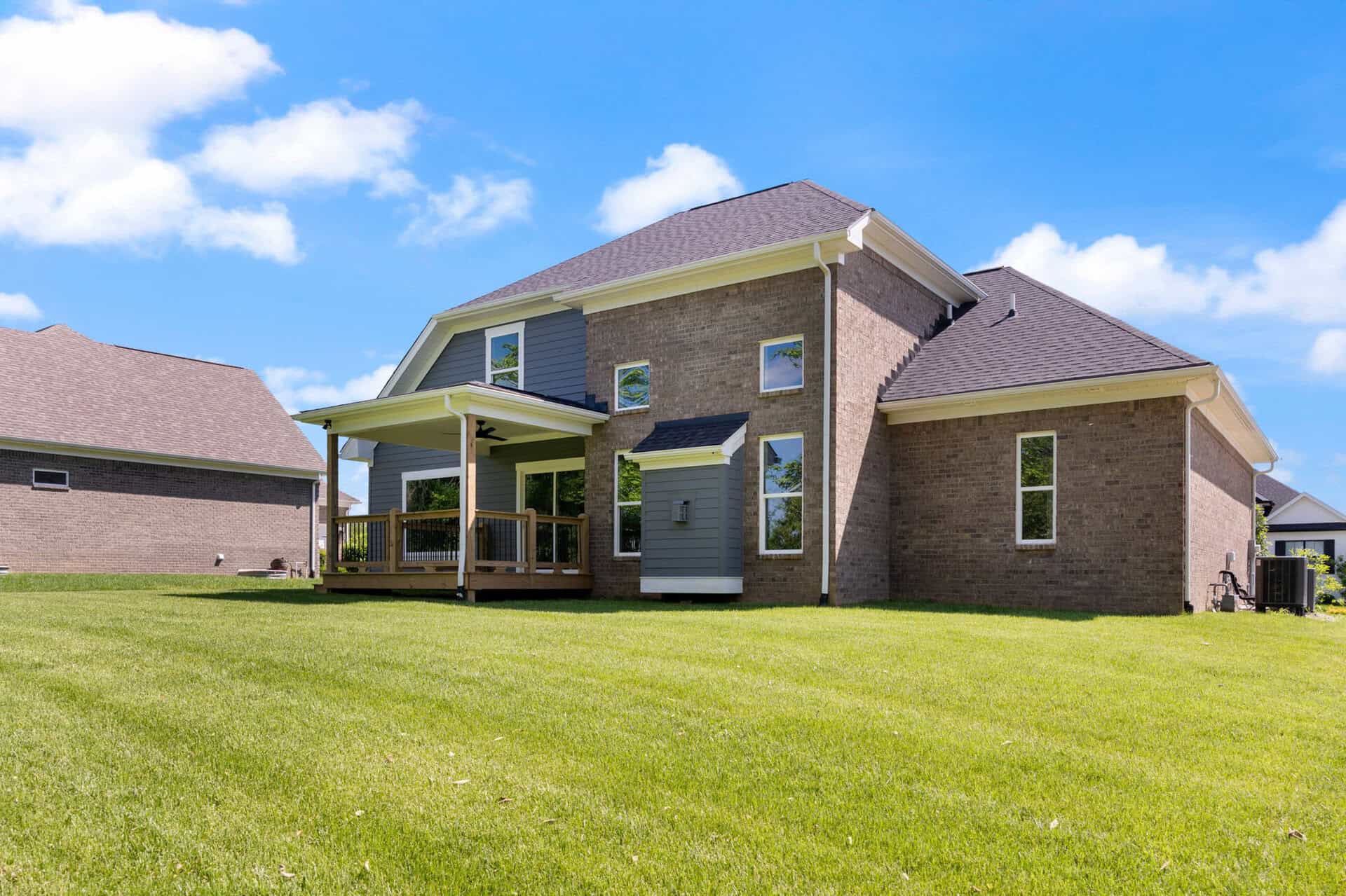 Modern brick home with a spacious backyard and a covered porch under a blue sky.