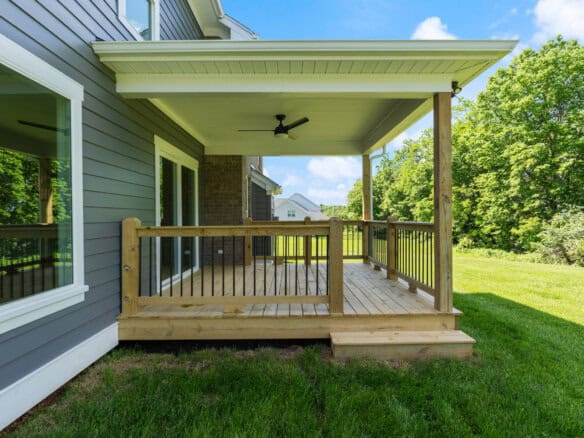 Newly built wooden deck with railing attached to a modern house in a green yard.