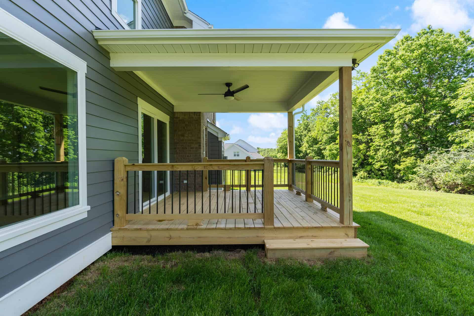 Newly built wooden deck with railing attached to a modern house in a green yard.