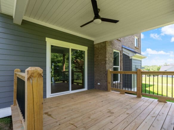 Wooden back deck attached to a gray house with sliding glass doors, a ceiling fan, and a wooden railing overlooking a yard.