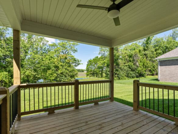 Covered porch with wooden railing overlooking green yard and trees.