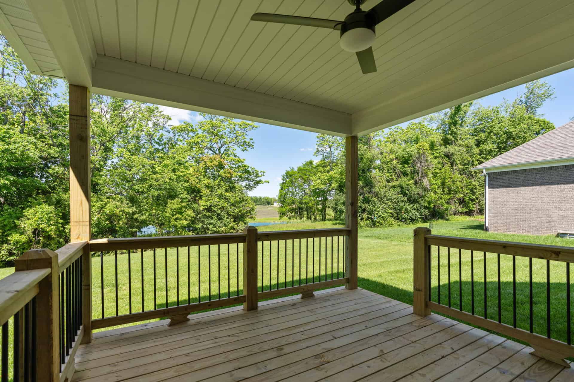 Covered porch with wooden railing overlooking green yard and trees.