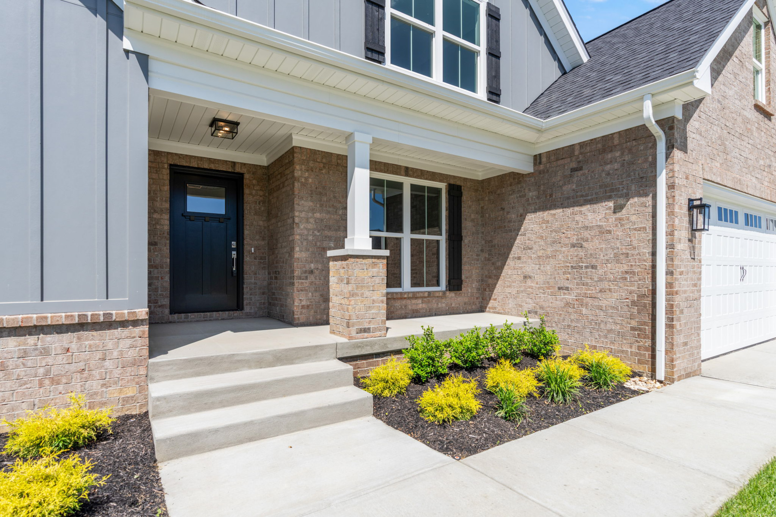 Modern house exterior with brick and siding, front steps, and landscaped yard.