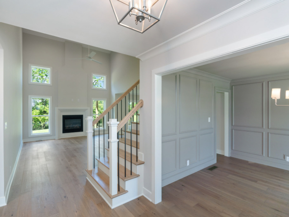 Bright living area with stairs, tall windows, and light-gray paneled walls